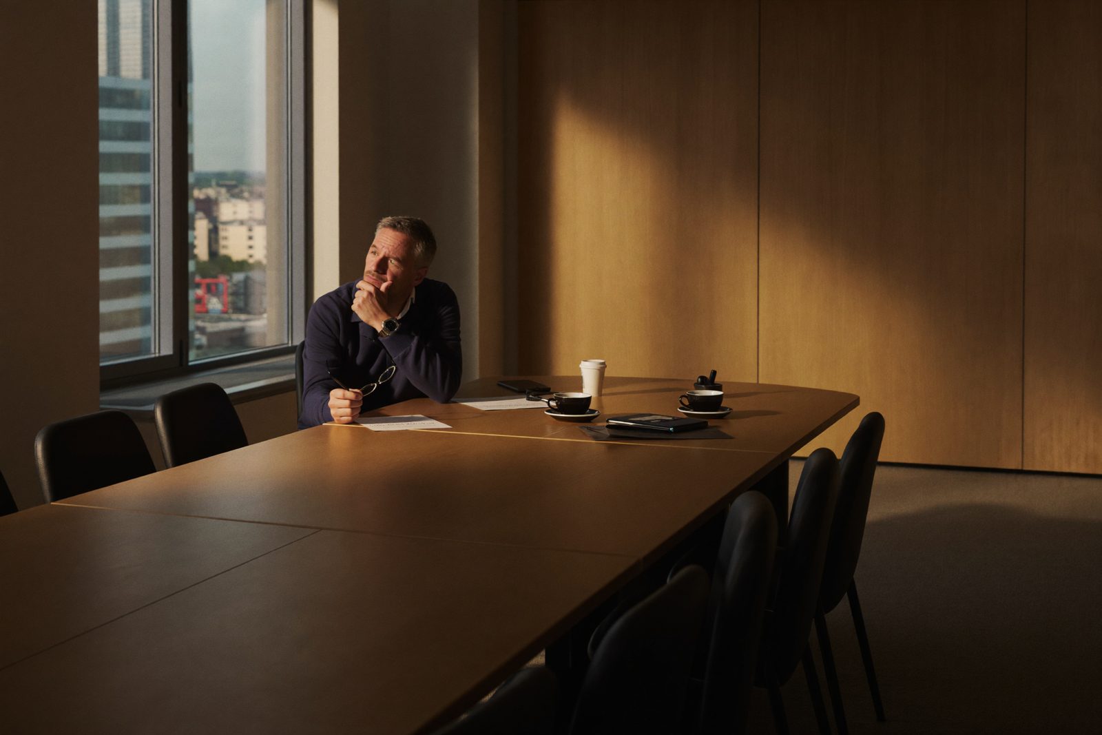 A CEO alone in a boardroom after the meeting, reading a report, unconvinced.
